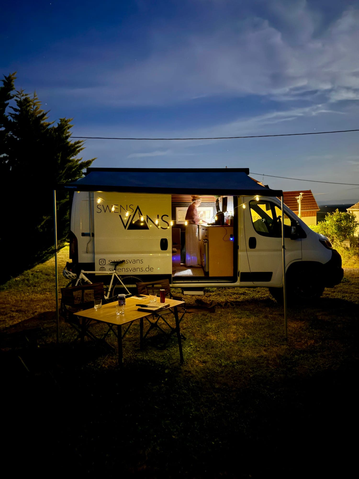 SVAN 01 Campervan bei Dämmerung mit Lichterkette und gedecktem Tisch